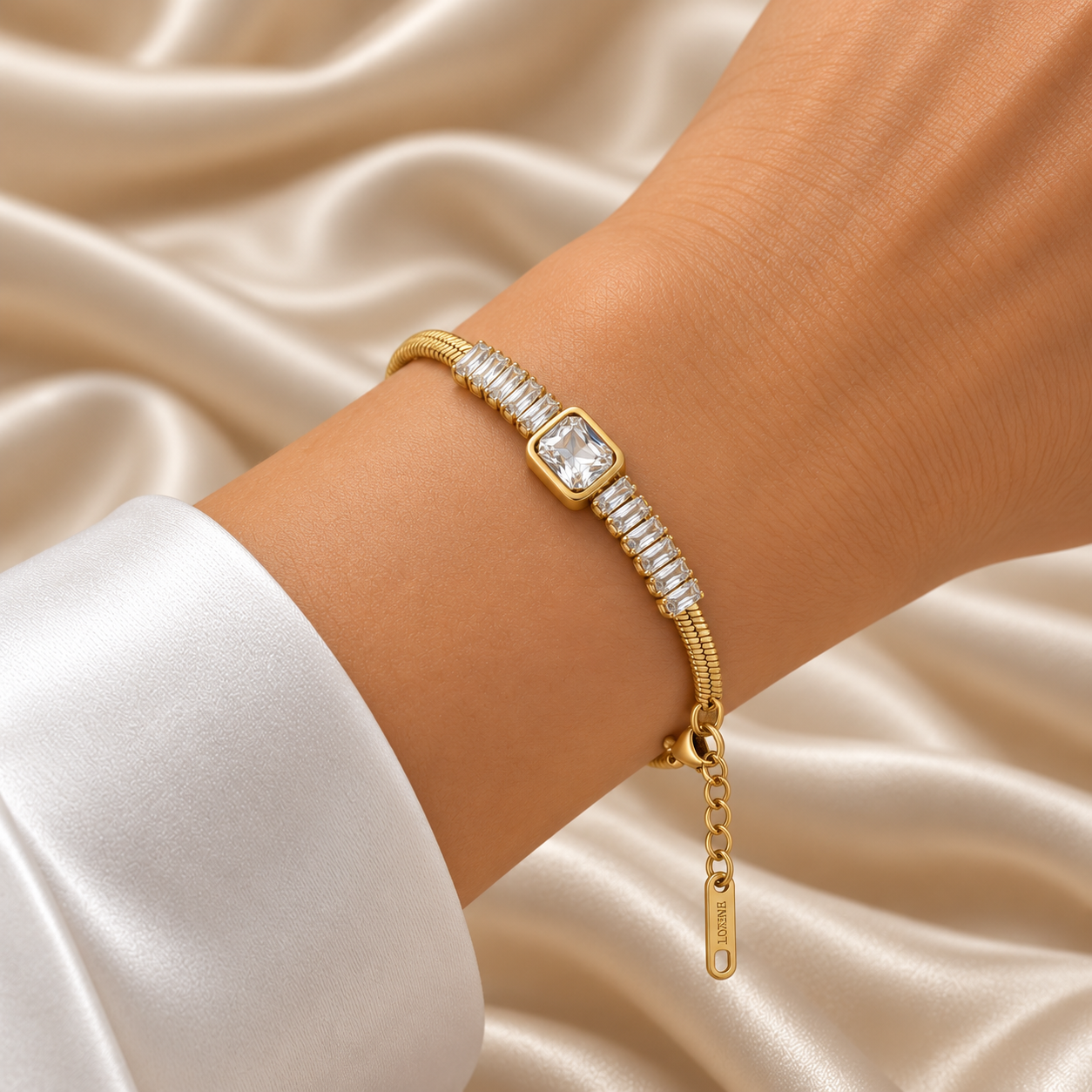 Gold Herringbone Chain Bracelet Baguette Crystal Station Emerald Bezel Centre - hero flat lay on cream satin: full bracelet showing wide flat warm 18K gold herringbone chain, continuous channel-set baguette white crystal zirconia station row across front half, large emerald-cut white crystal bezel centre focal at bracelet front, lobster clasp and extension chain, cream satin background