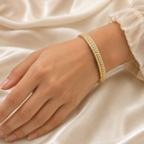 Gold-plated stainless steel bangle bracelet with clear stones worn on a wrist