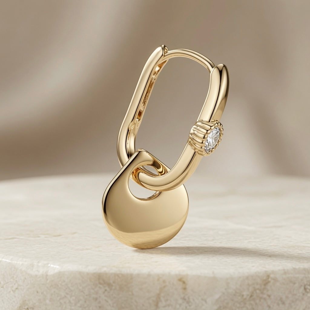 Disque Crystal Huggie Drop Earrings - single earring macro on marble showing interlocked disc construction and milgrain crystal bezel detail