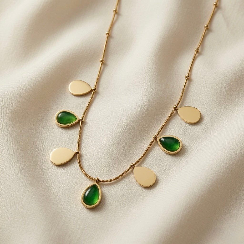 Pluie Verte Charm Necklace Gold & Emerald - flat lay on ivory silk showing seven alternating emerald crystal and gold mirror teardrop charms on satellite chain