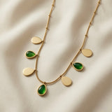 Pluie Verte Charm Necklace Gold & Emerald - flat lay on ivory silk showing seven alternating emerald crystal and gold mirror teardrop charms on satellite chain