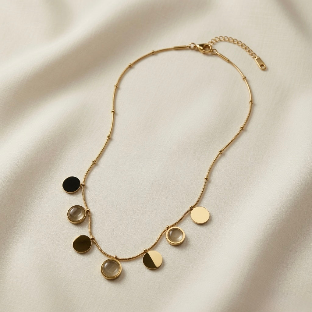 Sept Lunes Disc Station Necklace - full flat lay on ivory silk showing complete satellite chain with lobster clasp, curb extender and all seven alternating gold disc and moonstone circle pendants