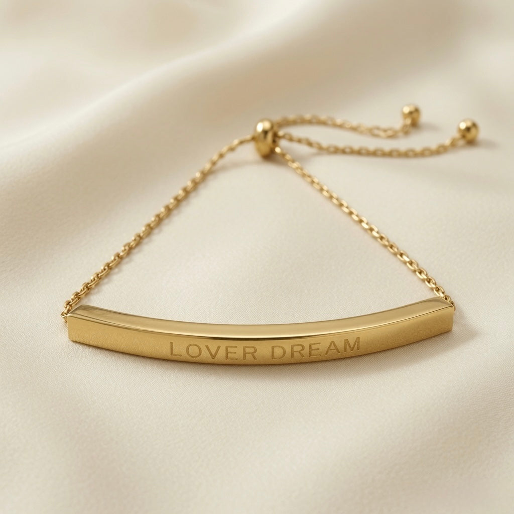 Lover Dream Curved Bar Bolo Bracelet - macro flat lay on ivory silk showing LOVER DREAM capital letter engraving in full detail on mirror-polished curved gold bar