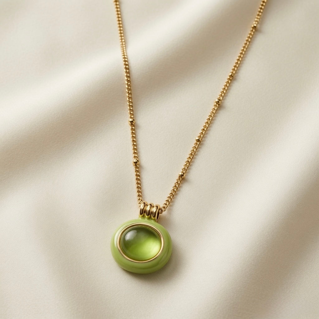 Pistache Cabochon Pendant Necklace - pendant close-up on ivory silk showing pistachio enamel frame, gold bezel and translucent olive crystal glow