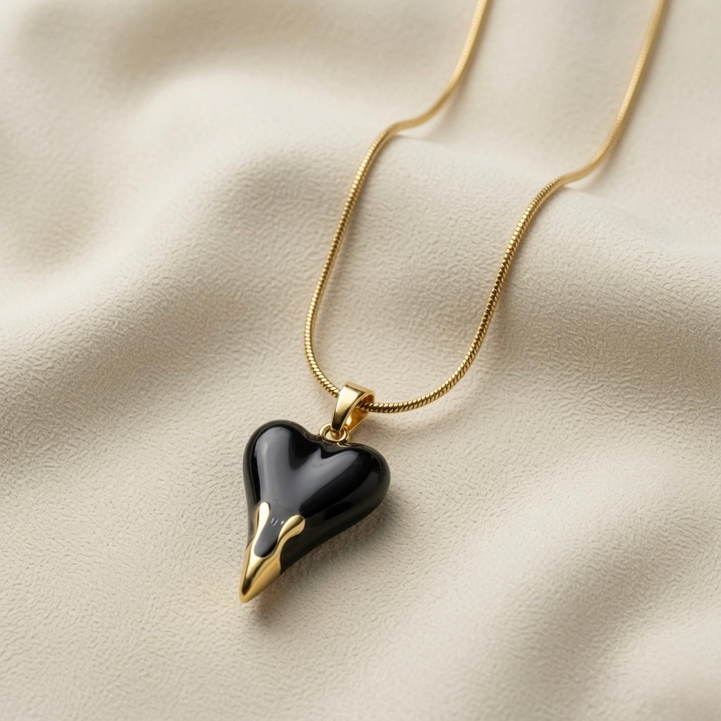 Coeur Noir Pendant Necklace - close-up on ivory silk showing black enamel heart side profile, gold drip tips at point and gold bail detail