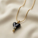 Coeur Noir Pendant Necklace - close-up on ivory silk showing black enamel heart side profile, gold drip tips at point and gold bail detail