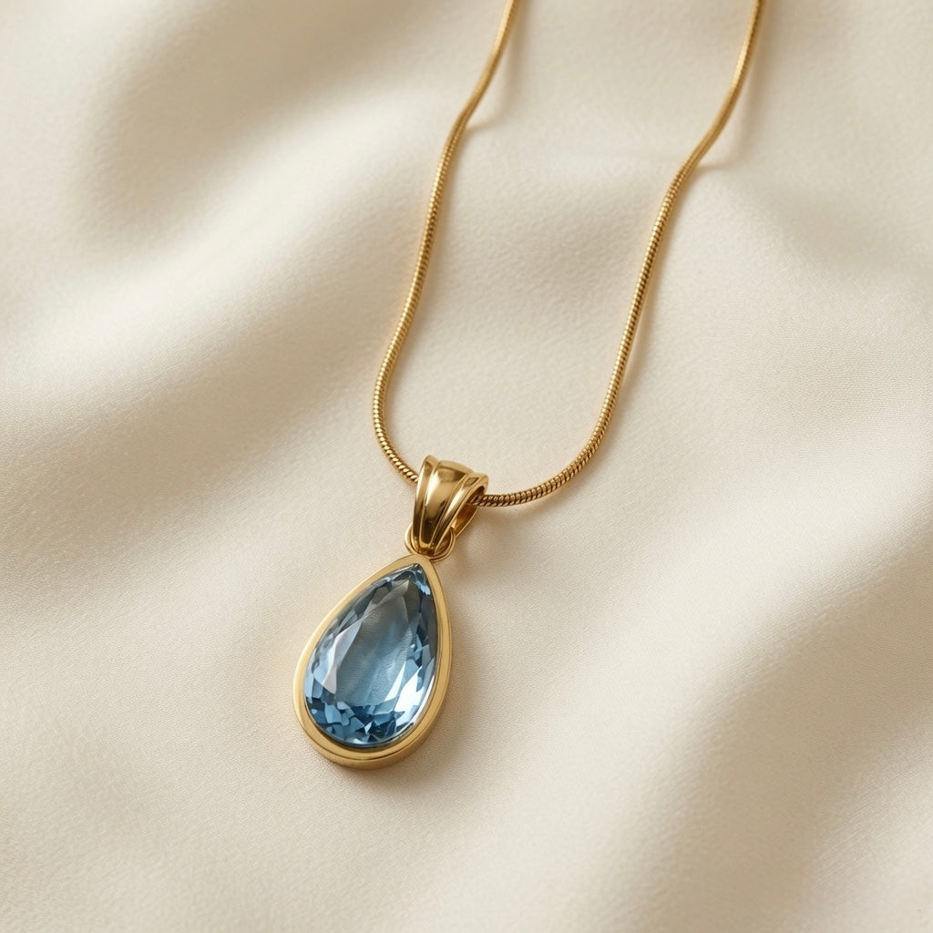 Larme Crystal Pear Pendant Necklace Aquamarine - close-up on ivory silk showing double-ridged gold bail, continuous bezel and aquamarine crystal facets