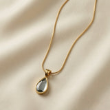 Larme Crystal Pear Pendant Necklace Smoky Grey - flat lay on ivory silk showing smoky grey mirror pear crystal in gold bezel on flat snake chain