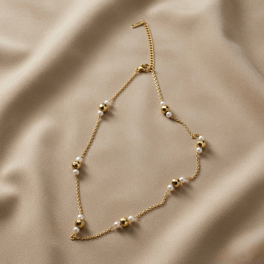 Perle Dorée Station Necklace - full flat lay on taupe silk showing alternating faceted gold disco beads and freshwater pearls on cable chain