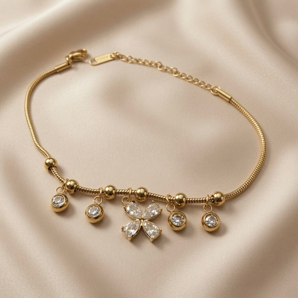 Fleur Cristal Fringe Drop Snake Chain Bracelet - flat lay on ivory silk showing round snake chain with five-drop crystal fringe: central four-petal marquise crystal flower flanked by four bezel-set round crystal drops on gold ball station beads, lobster clasp and Svora logo bar tag on curb extender