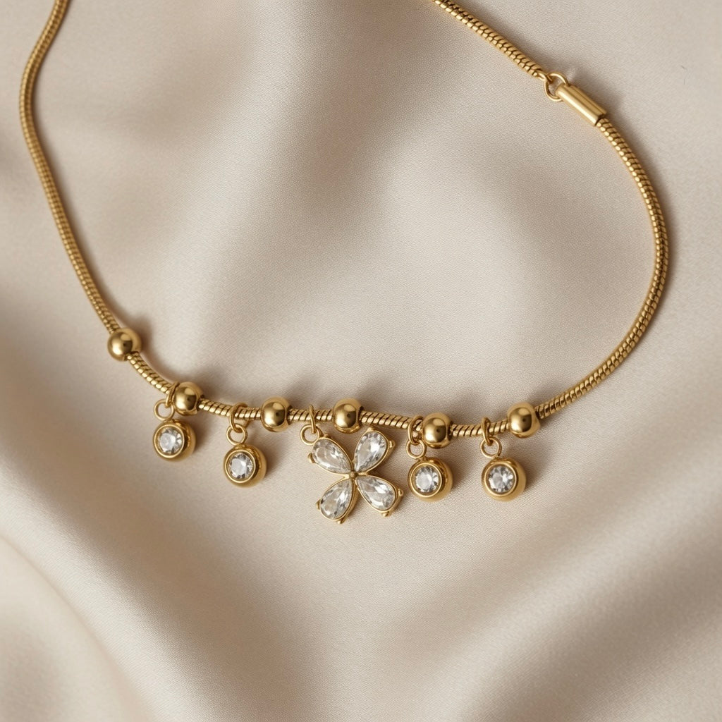 Fleur Cristal Fringe Drop Snake Chain Bracelet - macro close-up on ivory silk showing central four-petal marquise crystal flower in cross formation, four flanking round crystal zirconia drops in gold bezels and gold ball station beads on snake chain