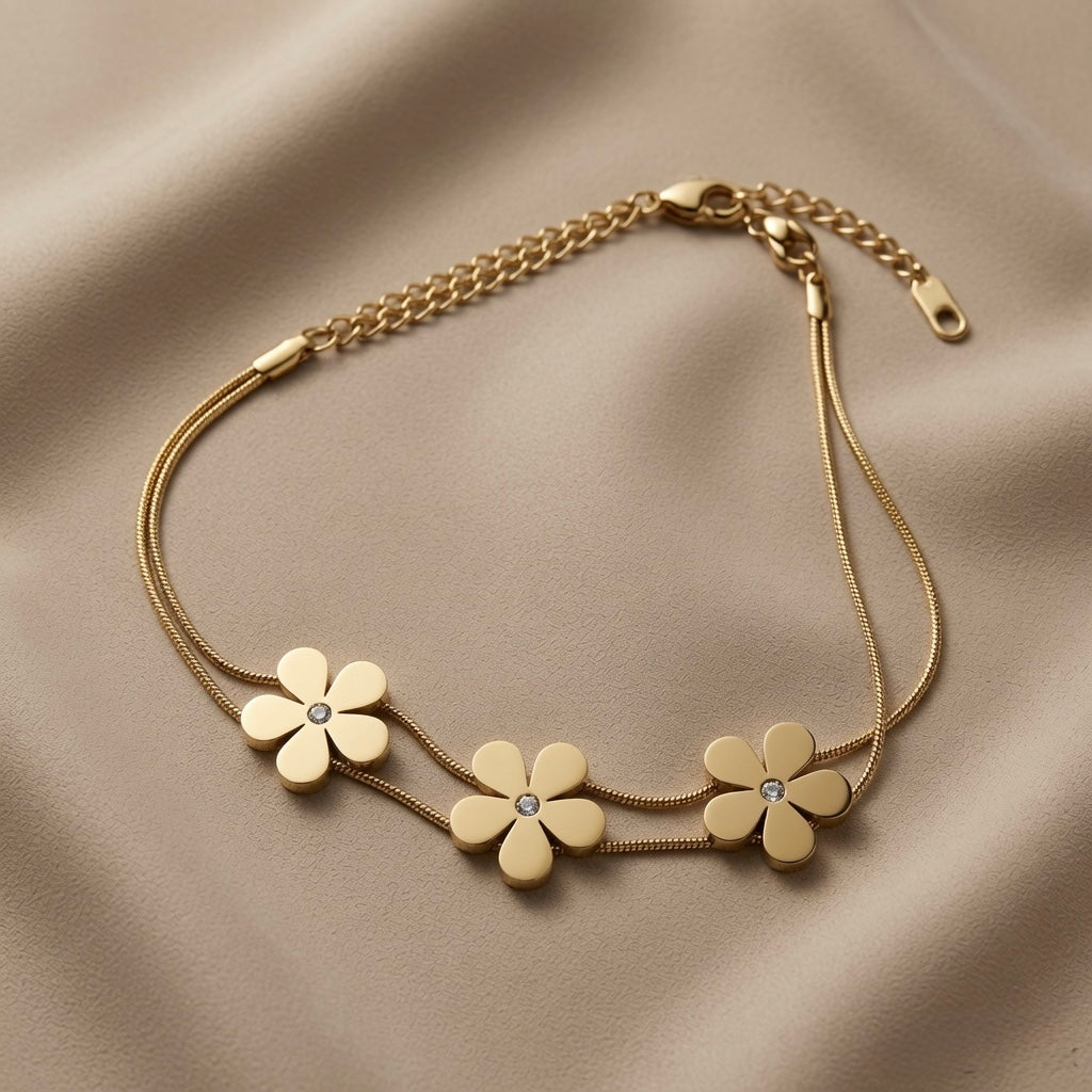 Trois Fleurs Double Snake Chain Bracelet in All Gold - flat lay on taupe silk showing three matte-satin gold daisy flowers with crystal zirconia centres threaded on double flat snake chain with lobster clasp and curb extender