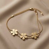 Trois Fleurs Double Snake Chain Bracelet in All Gold - flat lay on taupe silk showing three matte-satin gold daisy flowers with crystal zirconia centres threaded on double flat snake chain with lobster clasp and curb extender