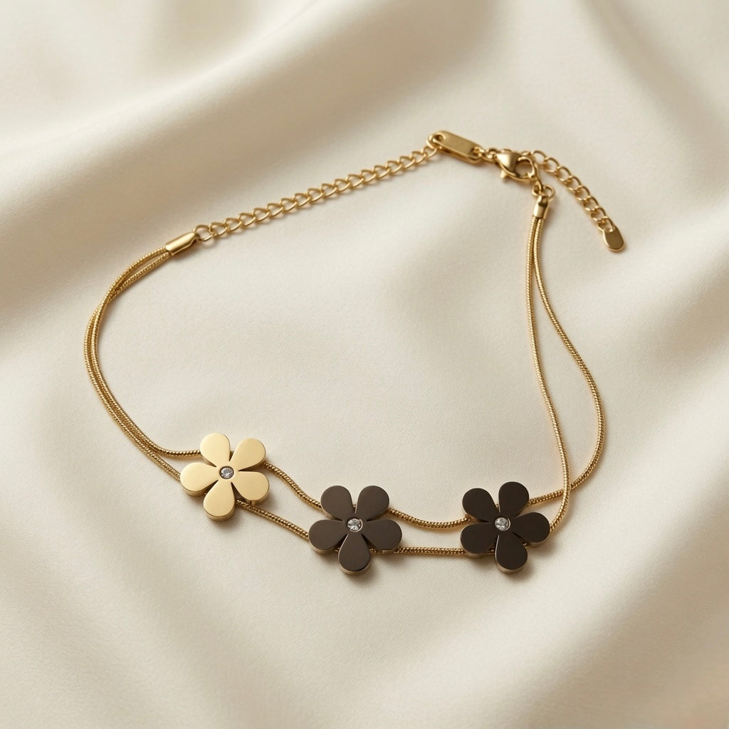 Trois Fleurs Double Snake Chain Bracelet Gold & Noir colourway - flat lay on ivory silk showing one gold daisy and two matte black daisy flowers with crystal centres on double gold snake chain