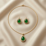 Impériale Jade Pavé Jewellery Set - flat lay on ivory silk showing matching pendant necklace and stud earrings with emerald green cabochon and pavé double halo