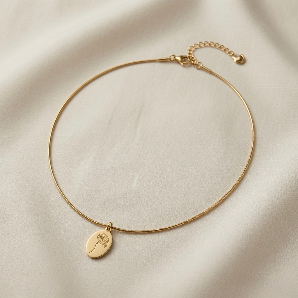 Fleur Gravée Oval Medallion Necklace - full flat lay on ivory silk showing smooth matte gold oval medallion with botanical engraving on flat snake chain