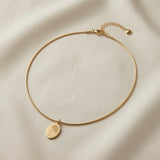 Fleur Gravée Oval Medallion Necklace - full flat lay on ivory silk showing smooth matte gold oval medallion with botanical engraving on flat snake chain
