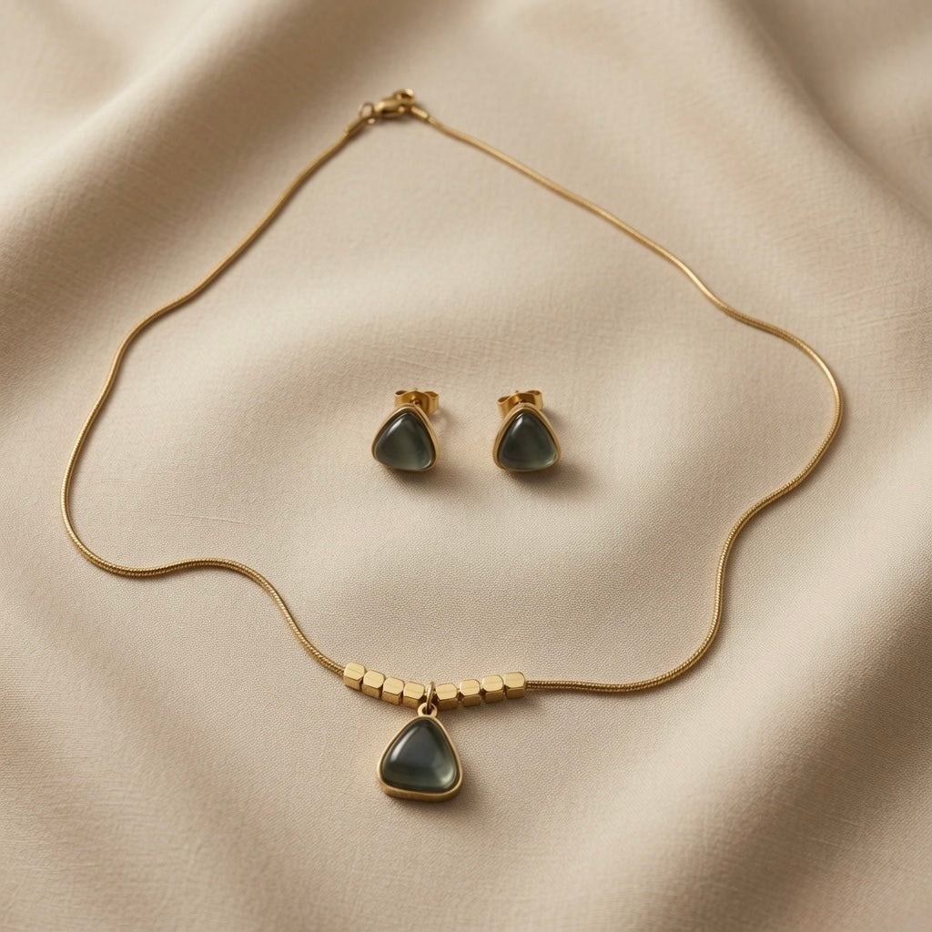 Orage Bleu Triangle Jewellery Set - full flat lay on ivory silk showing matching pendant necklace with hexagonal gold beads and triangle stud earrings in slate blue-grey cabochon