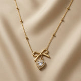 Noeud Coeur Crystal Bow Necklace - full flat lay on champagne silk showing complete satellite ball chain, lobster clasp extender, gold bow and crystal heart pendant