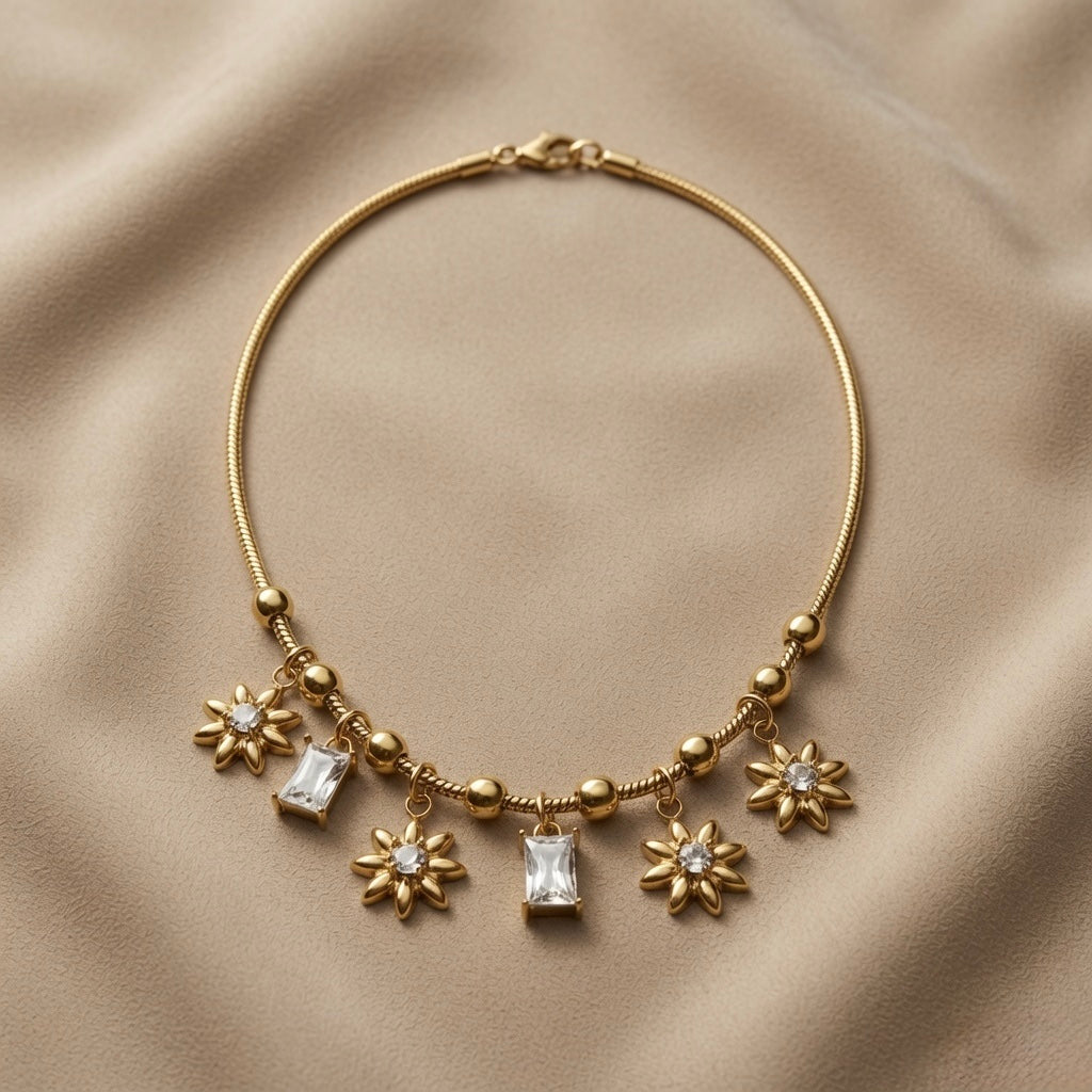 Soleil Baguette Fringe Charm Set necklace - flat lay on taupe silk showing round snake chain with alternating gold ball and rope barrel stations, three sculptural eight-petal gold sunflower charms with crystal centres alternating with two baguette crystal zirconia drops in four-prong gold mounts, lobster clasp