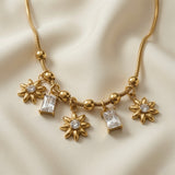 Soleil Baguette Fringe Charm Set necklace - macro close-up on ivory silk showing three ridged gold sunflower charms with round crystal centres and two emerald-cut baguette crystal drops in four-prong settings on alternating ball and barrel station snake chain