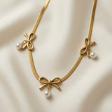 Trois Noeuds Pearl Herringbone Necklace - flat lay on ivory silk showing all three gold bows with pearl drops evenly spaced across herringbone chain