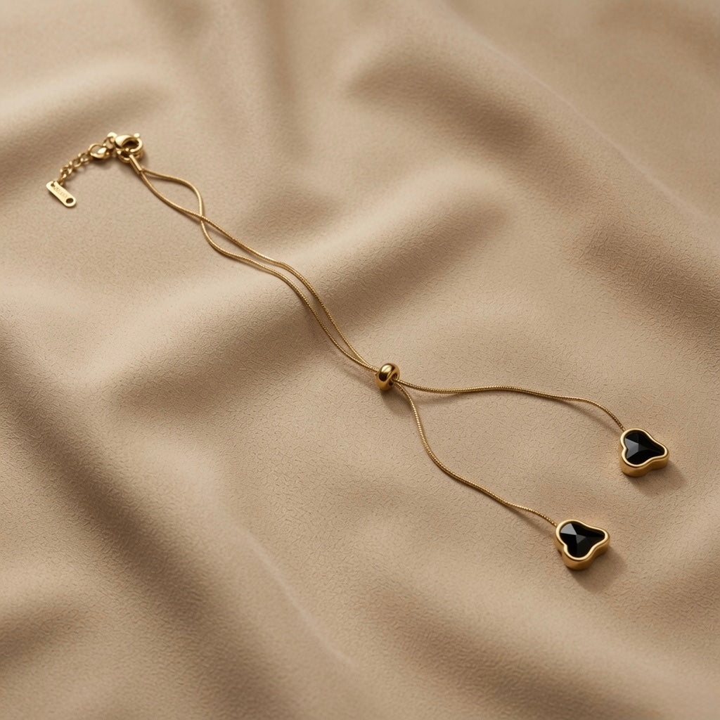 Coeur Noir Bolo Lariat Necklace - full flat lay on taupe silk showing complete round snake chain, lobster clasp extender, gold ball slider and two black crystal heart drops at tail ends