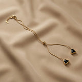 Coeur Noir Bolo Lariat Necklace - full flat lay on taupe silk showing complete round snake chain, lobster clasp extender, gold ball slider and two black crystal heart drops at tail ends