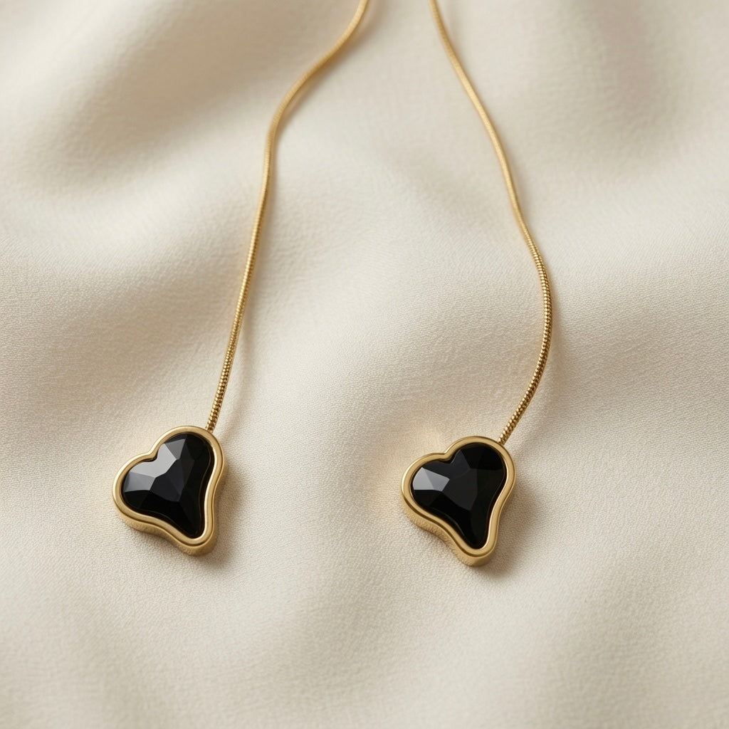 Coeur Noir Bolo Lariat Necklace - macro close-up on ivory silk showing two faceted black crystal hearts in smooth gold bezels side by side, rose-cut dark fire faceting detail