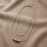 Trio Ovale Double Layer Snake Chain Necklace - flat lay on taupe silk showing double snake chain with three mirror-polished gold oval barrel beads on lower chain