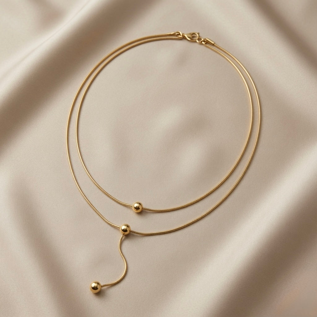 Sphère Lariat Double Layer Snake Chain Necklace - full flat lay on ivory silk showing double snake chain, three polished gold sphere beads and sinuous lariat drop tail