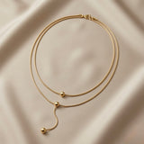 Sphère Lariat Double Layer Snake Chain Necklace - full flat lay on ivory silk showing double snake chain, three polished gold sphere beads and sinuous lariat drop tail