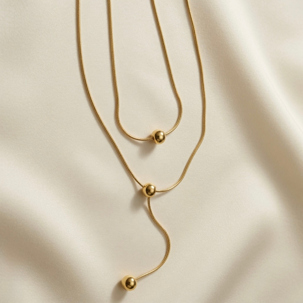 Sphère Lariat Double Layer Snake Chain Necklace - close-up flat lay on ivory silk showing sliding sphere mechanism, station sphere and lariat drop with terminating gold ball