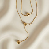 Sphère Lariat Double Layer Snake Chain Necklace - flat lay on ivory silk showing lariat drop S-curve, sliding sphere and terminating gold ball detail