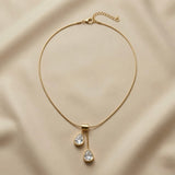 Duo Larme Crystal Asymmetric Pendant Necklace - full flat lay on champagne silk showing complete snake chain with lobster clasp extender, rectangular gold bail and two asymmetric white crystal pear pendants