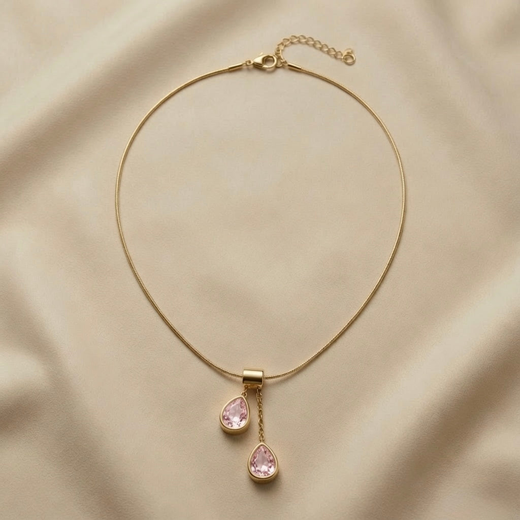 Duo Larme Rose Asymmetric Pendant Necklace - full flat lay on champagne silk showing complete snake chain with lobster clasp extender, rectangular gold bail and two asymmetric blush rose pear crystal pendants