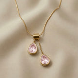 Duo Larme Rose Asymmetric Pendant Necklace - close-up on champagne silk showing rectangular gold bail, upper blush rose pear crystal on jump ring and lower pear on cable chain drop