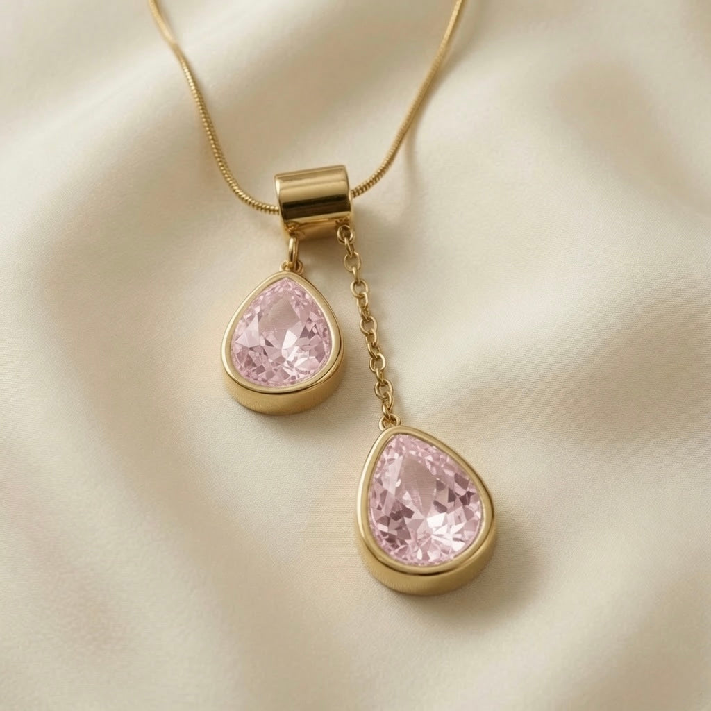Duo Larme Rose Asymmetric Pendant Necklace - macro close-up on ivory silk showing two bezel-set pear-cut rose crystals at asymmetric heights, morganite-pink facets and warm gold bezels in full detail