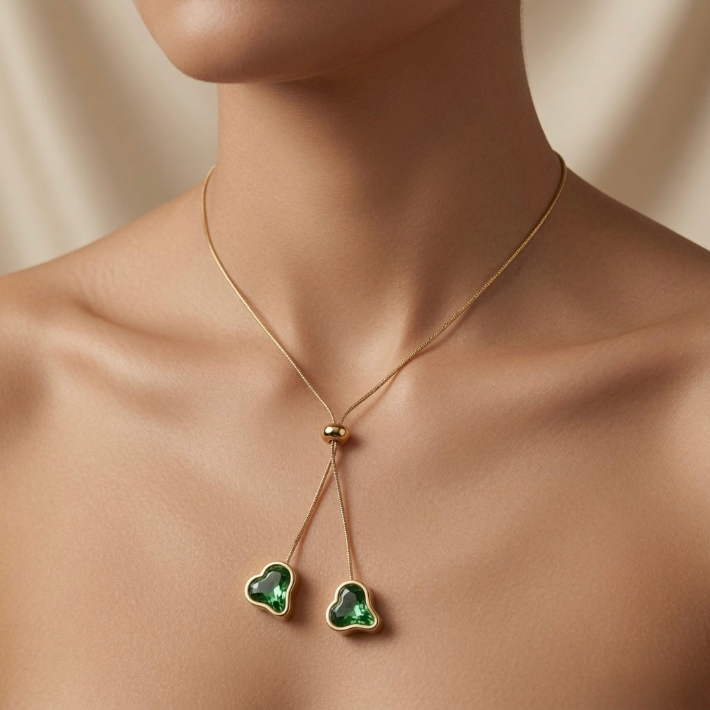 Émeraude Coeur Lariat Necklace - worn on model décolletage showing two emerald hearts resting below collarbone on gold snake chain