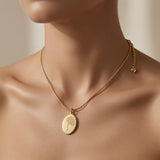 Fleur Gravée Oval Medallion Necklace - worn on mannequin collarbone showing matte gold oval pendant at chest centre, flat snake chain and gold heart charm on curb extender