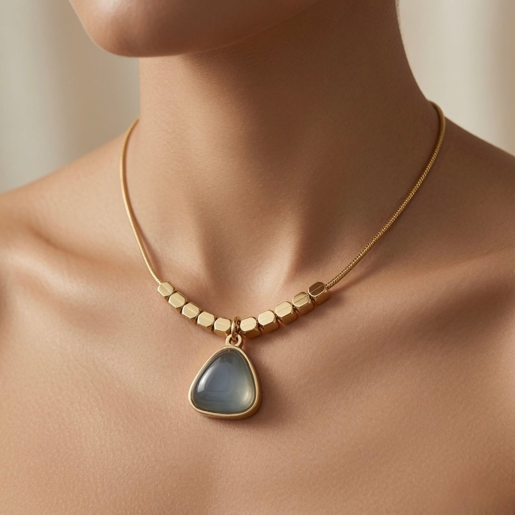 Orage Bleu Triangle Necklace - worn on mannequin collarbone showing slate blue triangle pendant at chest centre, hexagonal gold bead row and flat snake chain