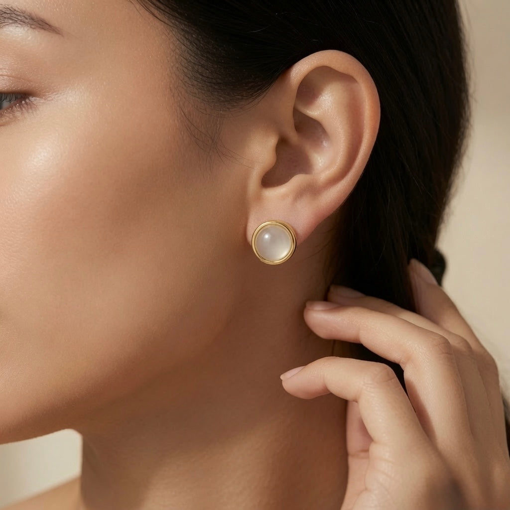 Lune Blanche Cabochon Earrings - worn on model ear showing round white moonstone cabochon stud in double-ridged gold bezel at lobe with soft milky iridescent glow