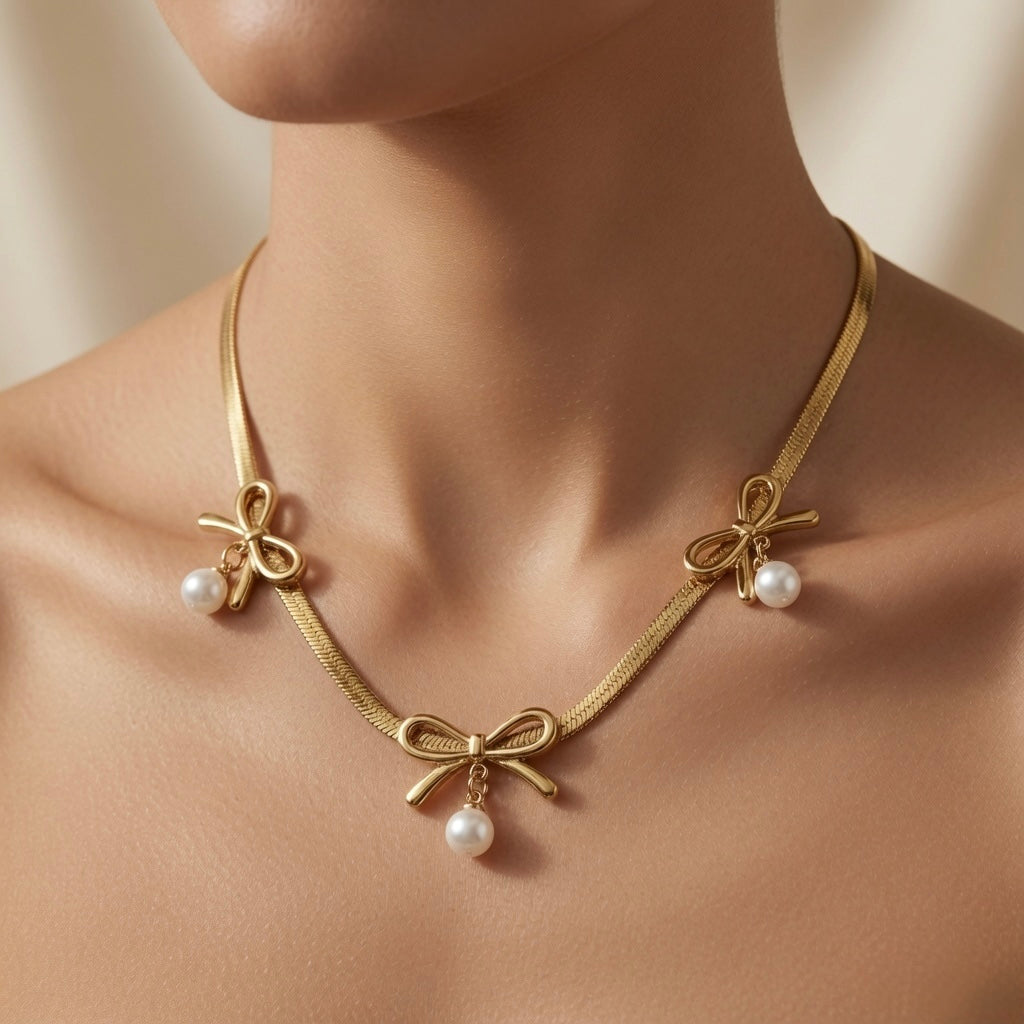 Trois Noeuds Pearl Herringbone Necklace - worn on mannequin collarbone showing three gold bows and three pearl drops fanning across chest on wide flat herringbone chain