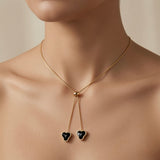 Coeur Noir Bolo Lariat Necklace - worn on mannequin collarbone showing gold ball slider at collarbone, two snake chain tails descending to sternum with two black crystal hearts side by side at chest centre
