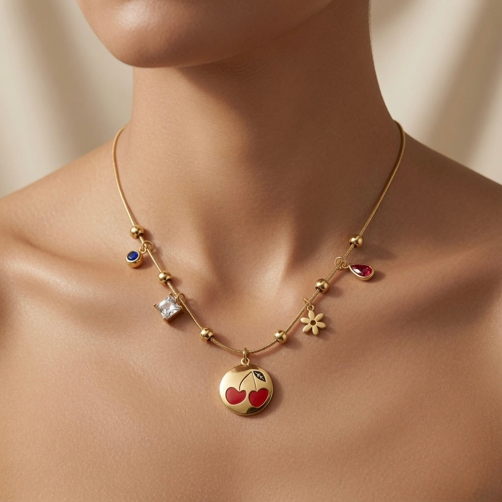 Cerise Charm Station Necklace - worn on mannequin collarbone showing cherry medallion at chest centre, four satellite charms fanning across collarbone on gold ball station snake chain