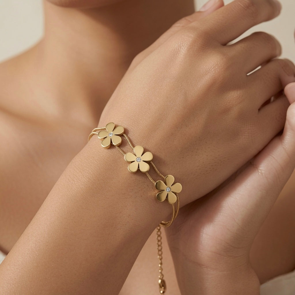 Trois Fleurs Double Snake Chain Bracelet in All Gold - worn on model wrist showing three matte-satin gold daisy flowers with crystal centres fanning across wrist on double snake chain, curb extender visible
