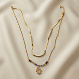 Hamsa Gemstone Layer Necklace Set - full flat lay on ivory silk showing two necklaces: flat herringbone snake chain above and multicolour gemstone bead station chain with large multicolour pavé Hamsa hand pendant below, both with lobster clasps and curb extenders