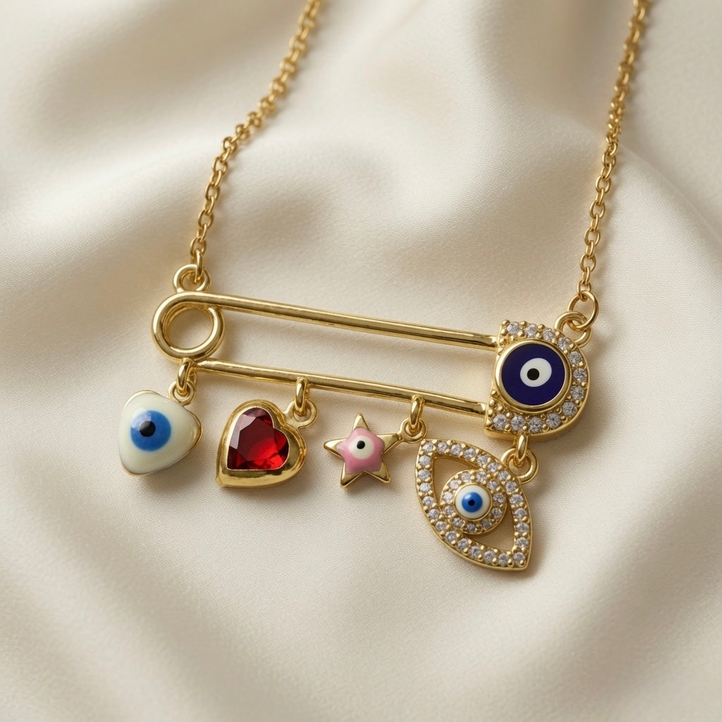 Amour Nazar Pin Charm Necklace - macro close-up on ivory silk showing large gold safety pin with navy pavé evil eye at clasp end and five sliding charms: white enamel evil eye heart, ruby red faceted crystal heart in gold bezel, pink enamel star, large pavé crystal marquise evil eye with blue centre