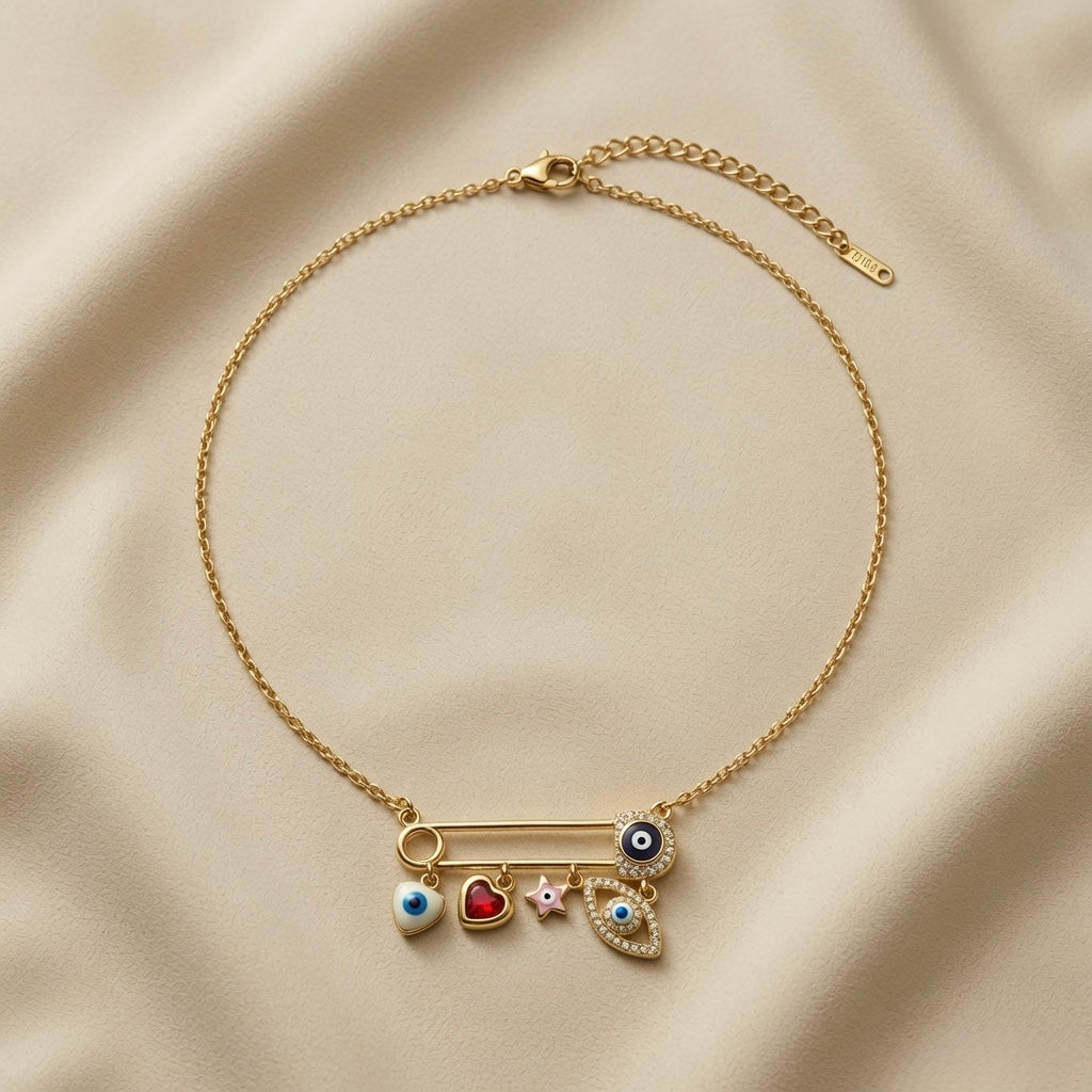 Amour Nazar Pin Charm Necklace - full flat lay on ivory silk showing complete gold cable chain with lobster clasp and curb extender, large gold safety pin centrepiece with navy pavé evil eye clasp and five sliding charms: evil eye heart, ruby heart, pink star and pavé marquise evil eye