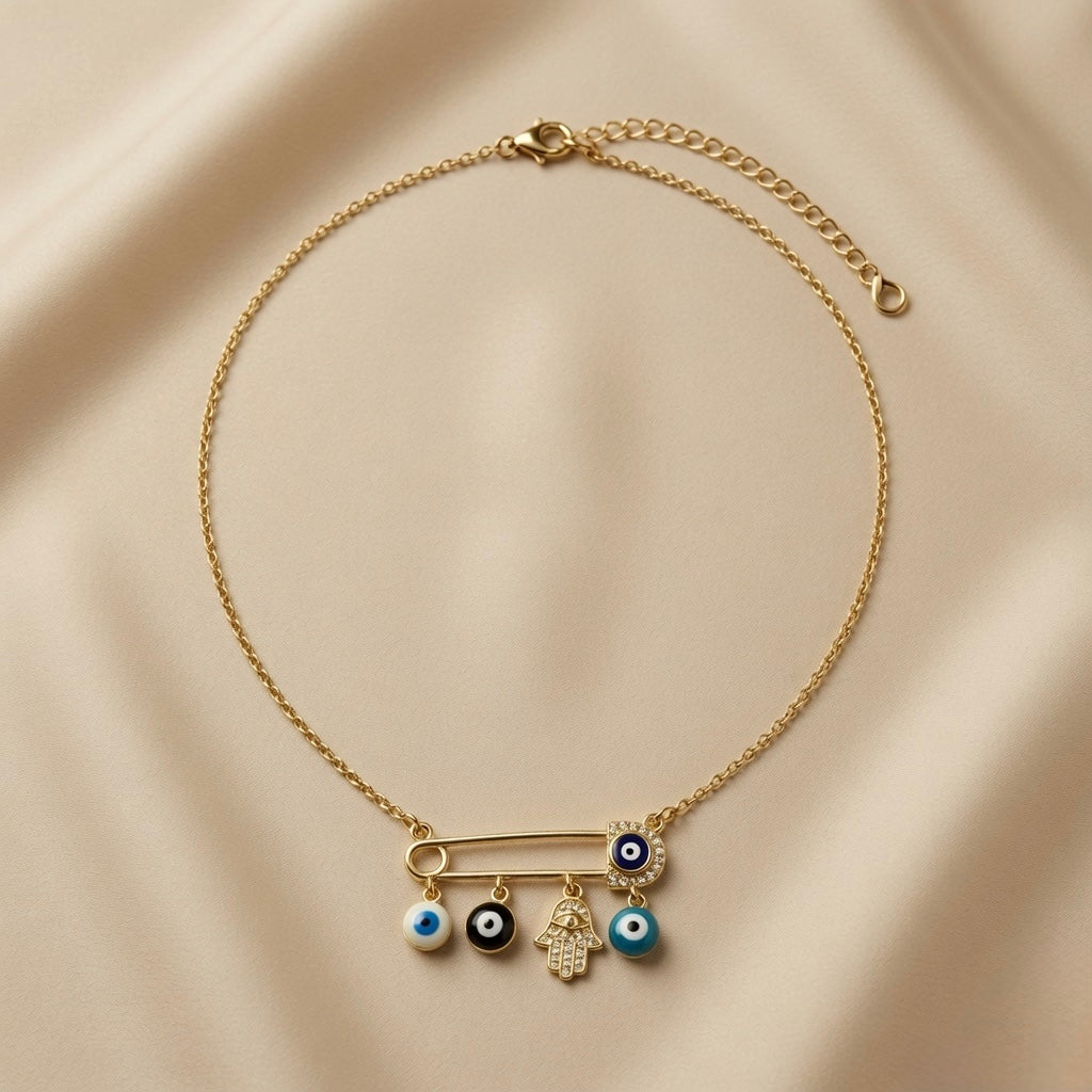 Nazar Pin Charm Necklace - full flat lay on ivory silk showing complete gold cable chain with lobster clasp and curb extender, large gold safety pin with navy pavé evil eye disc at clasp end and four sliding charms: white evil eye bead, black evil eye bead, pavé Hamsa hand and turquoise evil eye bead on pin bar